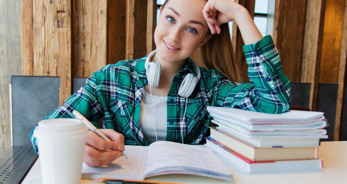 Kobieta na studiach podyplomowych siedzy przy biurku z kawą i robi notatki