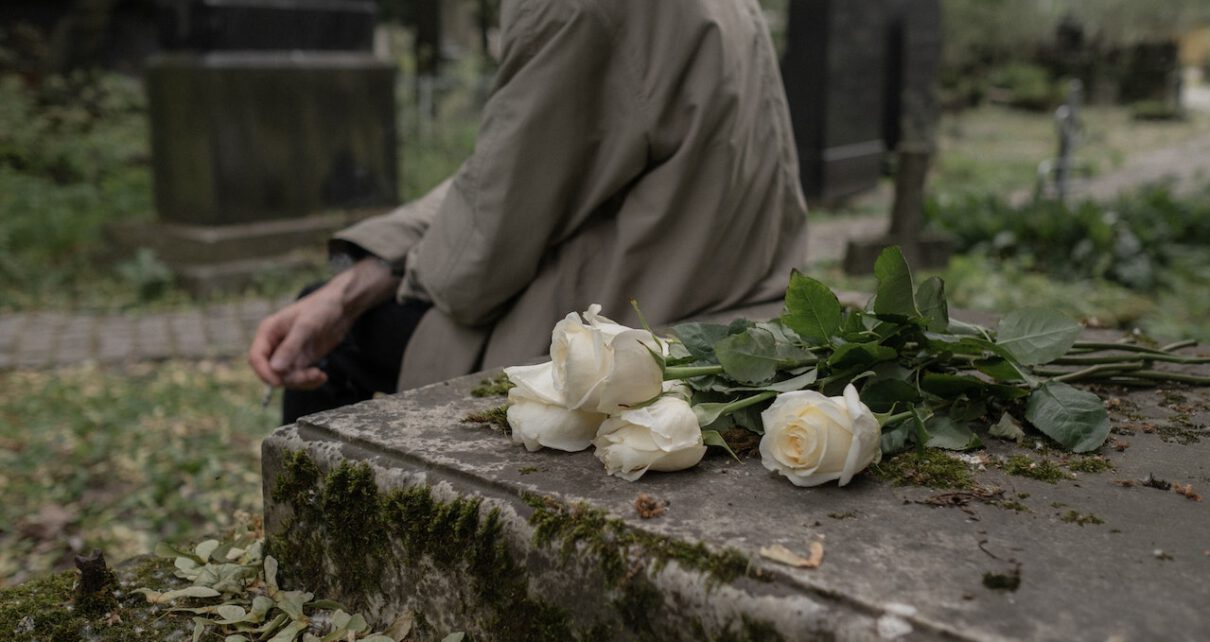 Mężczyzna siedzi na cmentarzu obok nagrobka