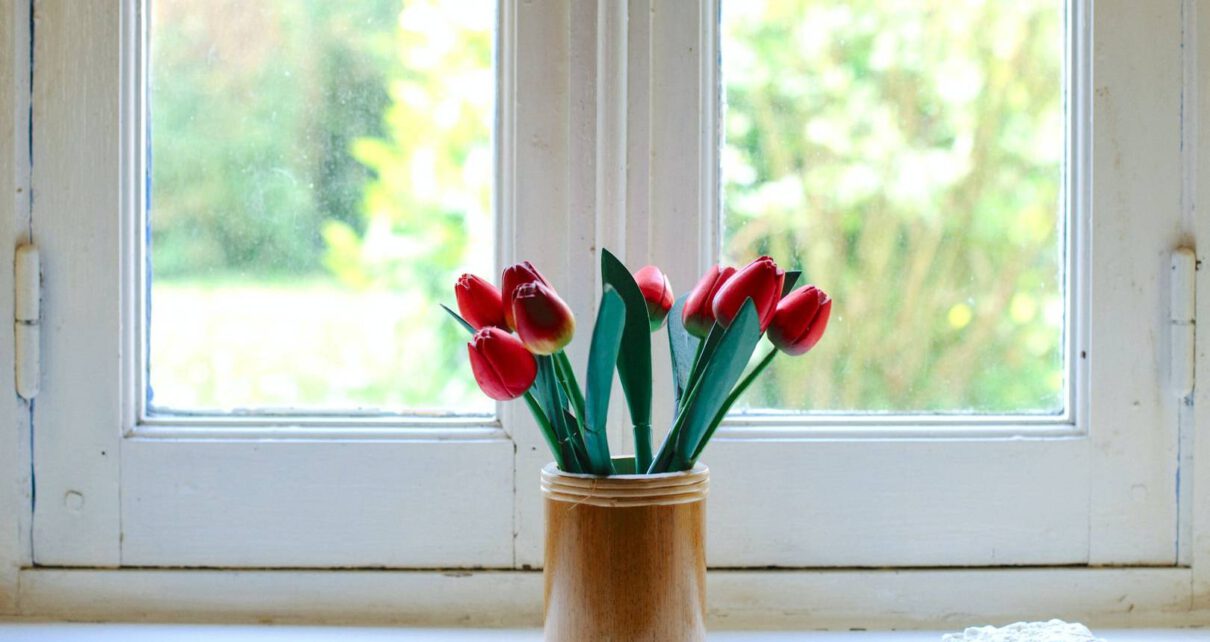 Kwiaty w wazonie stoją na parapecie obok drewnianego okna